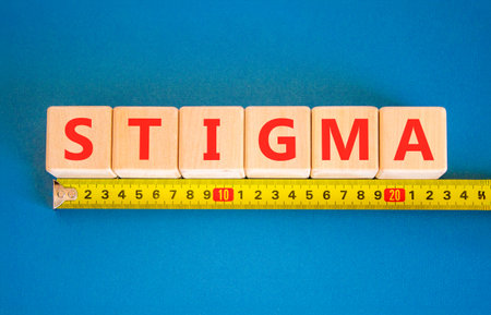 Stigma word symbol. Concept word Stigma on wooden blocks. Blue background. Yellow tape measure...