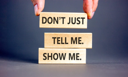Tell or show symbol. Concept words Do not just tell me, show me on beautiful wooden blocks. Beautiful gray background. Businessman's hand. Business tell or show concept. Copy space.の写真素材