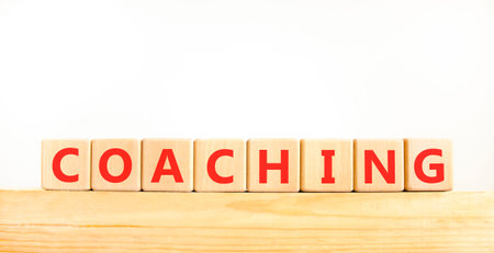 Coaching word symbol. Concept word Coaching on beautiful wooden blocks on wooden beam. Beautiful white background. Business support help coaching word concept. Copy space.の写真素材