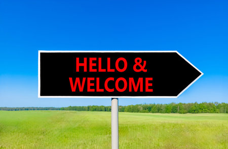 Hello and welcome symbol. Concept words Hello and welcome on beautiful black road sign. Beautiful blue sky green grass field background. Business hello and welcome concept. Copy space.の写真素材