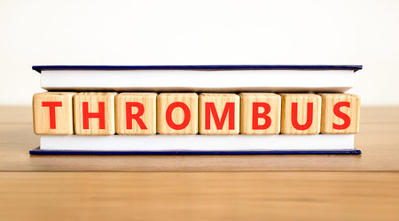 Thrombus word symbol. Concept word Thrombus on beautiful wooden blocks in beautiful book. Beautiful wooden table white background. Business medical support help thrombus word concept. Copy space.の写真素材