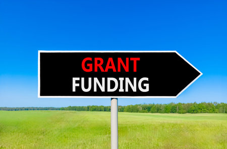 Grant funding symbol. Concept words Grant funding on beautiful black road sign. Beautiful blue sky...