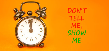 Tell or show symbol. Concept words Do not tell me, show me on beautiful orange paper. Beautiful orange paper background. Beautiful black alarm clock. Business tell or show concept. Copy space.の写真素材