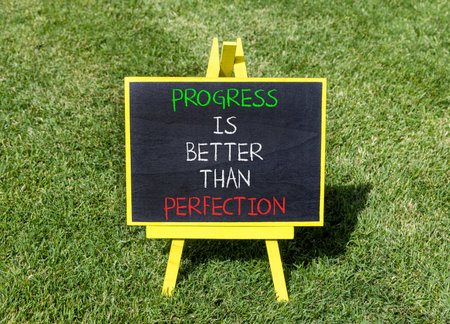 Progress or perfection words symbol. Concept words Progress is better than perfection on beautiful blackboard. Beautiful green grass background. Business progress or perfection concept. Copy space.の写真素材