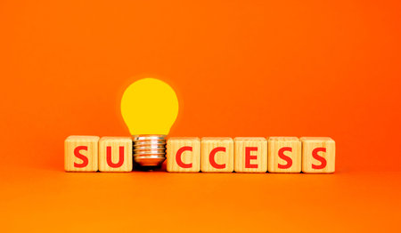 Successful success symbol. Concept word Success on beautiful wooden blocks. Beautiful orange background. Beautiful yellow light bulb. Business success or successful concept. Copy space.の写真素材