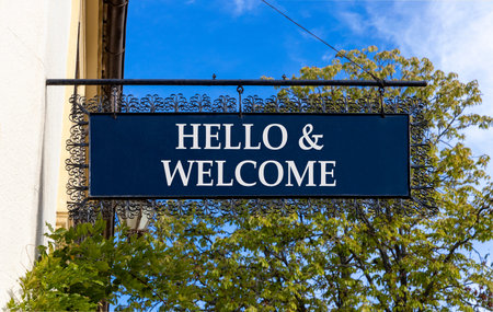 Hello and welcome symbol. Concept words Hello and welcome on beautiful big black road sign. Beautiful blue sky green trees background. Business hello and welcome concept. Copy space.