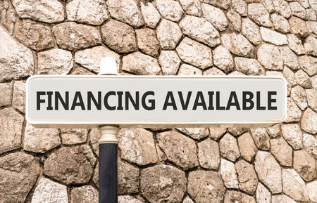 Financing available symbol. Concept words Financing available on beautiful big white road sign. Beautiful grey stone wall background. Business financing available concept. Copy space.