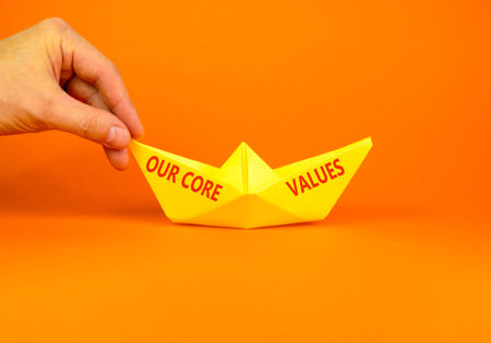 Our core values symbol. Concept words Our core values on beautiful yellow paper boat. Beautiful orange background. Businessman hand. Business our core values motivational support concept. Copy space.