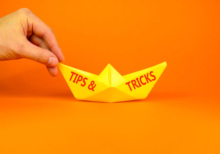 Tips and tricks symbol. Concept words Tips and tricks on beautiful yellow paper boat. Beautiful orange background. Businessman hand. Business tips and tricks motivational support concept. Copy space.