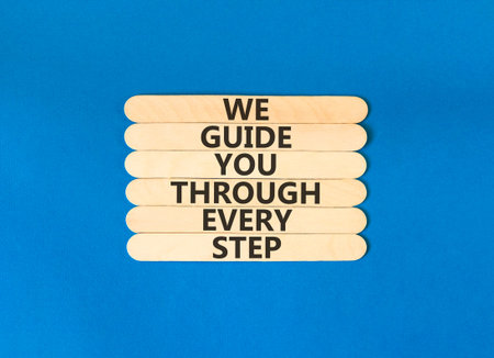 We guide you through every step symbol. Concept words We guide you through every step on wooden sticks. Beautiful blue paper background. Business We guide you through every step concept. Copy space.