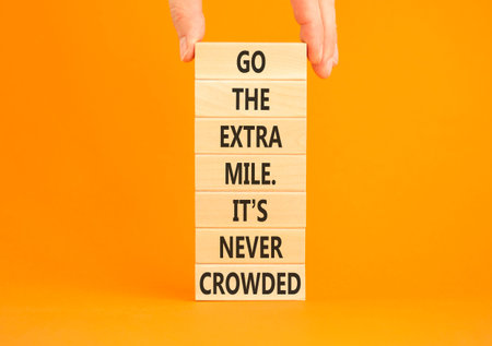 Go the extra mile symbol. Concept words Go the extra mile. It's never crowded on beautiful wooden blocks. Beautiful orange background. Businessman hand. Business go the extra mile concept. Copy space.