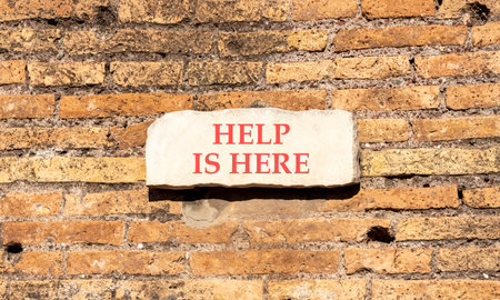 Help is here and support words symbol. Concept words Help is here on beautiful white sign plate. Beautiful brown brick wall background. Business help is here and support concept. Copy space.