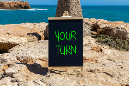 Your turn words symbol. Concept words Your turn on beautiful black blackboard. Beautiful stone blue sea blue sky background. Business your turn motivational support concept. Copy space.