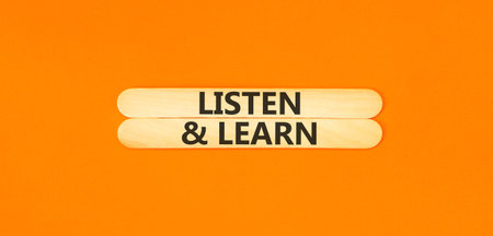 Listen and learn words symbol. Concept words Listen and learn on beautiful wooden sticks. Beautiful orange background. Business listen and learn support concept. Copy space.