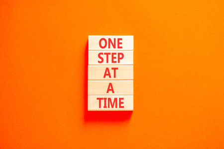 One step at a time symbol. Concept words One step at a time on beautiful wooden blocks. Beautiful orange background. Business and one step at a time concept. Copy space.