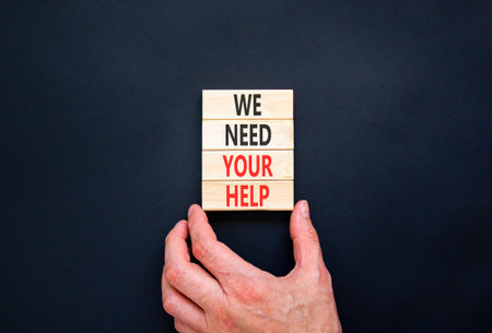 We need your help words symbol. Concept words We need your help on beautiful wooden blocks. Beautiful black background. Businessman hand. Business support we need your help concept. Copy space.