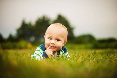Cute baby looking at camera and smiling while lying on the grass outdoors in sunlightの写真素材