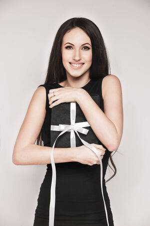 Young beautiful woman with long hair wearing black cocktail dress is holding elegantly wrapped gift.の写真素材