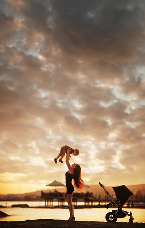 Young attractive mother and her baby boy having fun at sunset on the beach.の写真素材