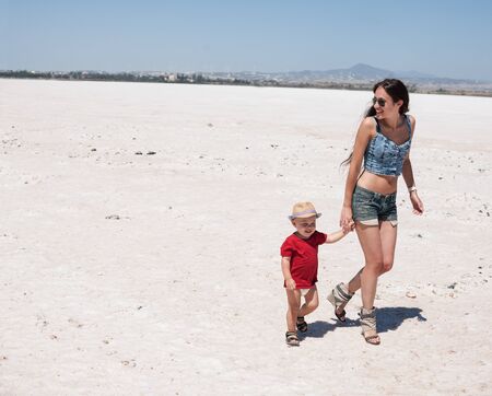 Young attractive mother and her baby boy having fun on the beach on bright sunny day.の写真素材