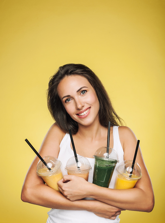 Young attractive brunette woman holding takeaway cups of smoothie. Happy girl posing on yellow background. Healthy eating concept.の写真素材