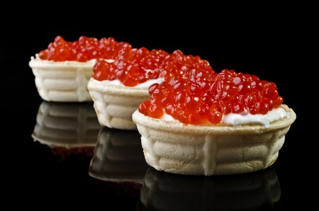 Delicatessen appetizer - red caviar in tartlet, isolated on a black backgroundの写真素材