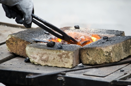 Hand blacksmith heats the metal in hot coals