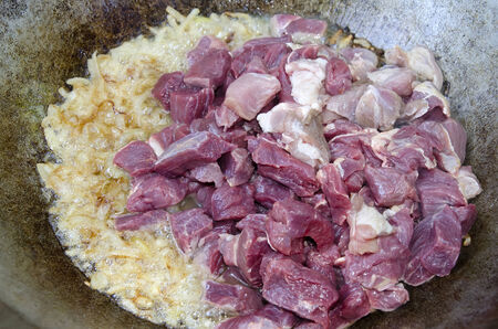 Preparation pilaf in a cauldron - Onions and chunks of beef stewed in a cauldronの写真素材