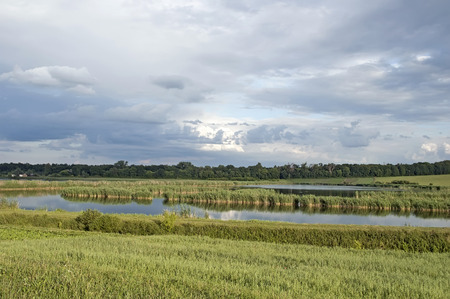 Beautiful rural landscape - pond on the edge of the forest and dramatic cloudsの写真素材