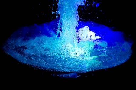 Flow blue water in the fountain at the night light. Isolated over blackの写真素材