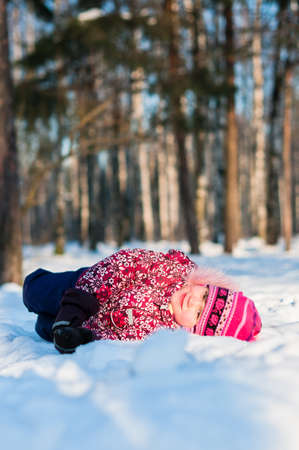Baby lays on snow in wood, looks and smileの写真素材