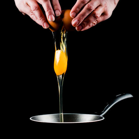 Yolk dropping in pan from cracked raw egg, divided by woman hands