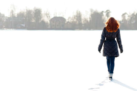 Pretty red haired girl walking on frozen lake and making footpathの写真素材