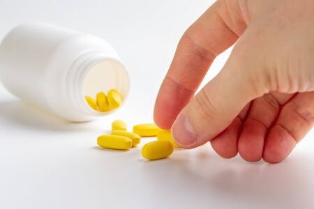 yellow pills and hand isolated on white backgroundの写真素材