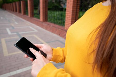 Young girl in a yellow sweater holds a phone and scrolls