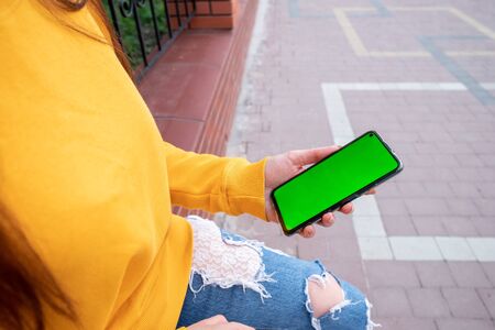 Young girl in a yellow sweater holds a phone with a green screenの写真素材