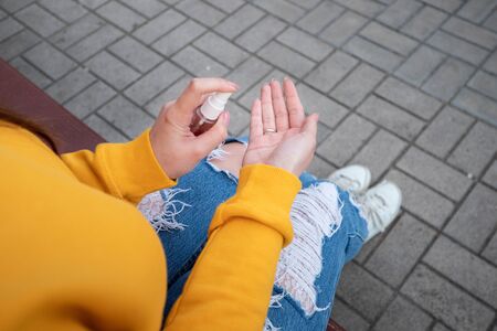 A young girl in a yellow sweater disinfects the hands with a spray sanitizerの写真素材