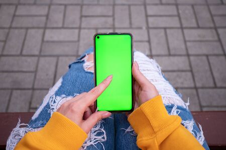 Young girl in a yellow sweater holds a phone with a green screenの写真素材