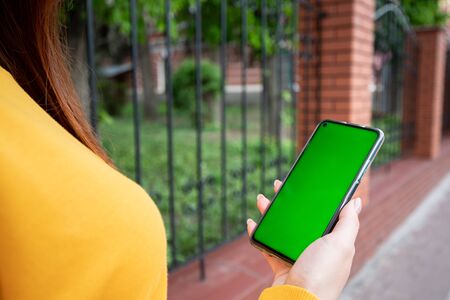 Young girl in a yellow sweater holds a phone with a green screenの写真素材
