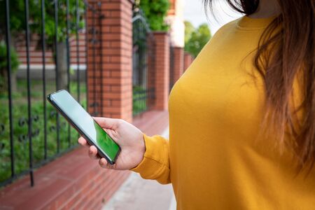 Young girl in a yellow sweater holds a phone with a green screenの写真素材