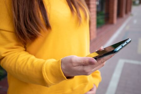 Young girl in a yellow sweater holds a smartphone on the streetの写真素材