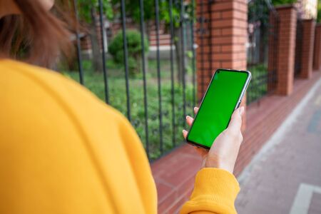 Young girl in a yellow sweater holds a phone with a green screenの写真素材