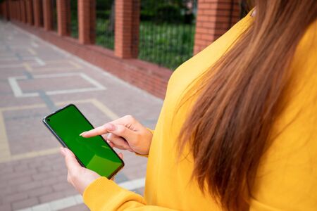 Young girl in a yellow sweater holds a phone with a green screen and scrollの写真素材