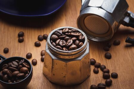 Coffee beans in a geyser coffee maker and on a wooden table with a cup on a platterの写真素材