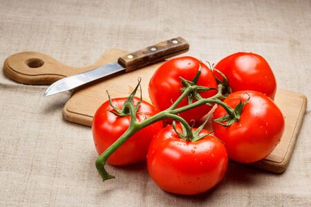 Juicy red tomatoes on a cutting board and a knifeの写真素材
