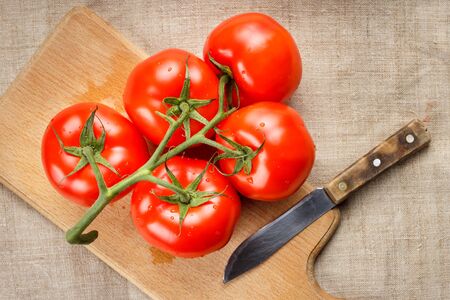 Juicy red tomatoes on a cutting board with a knife. Top view.の写真素材