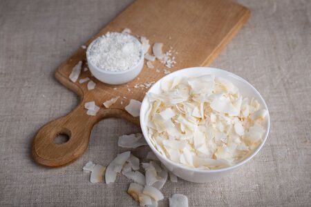 Coconut chips and shavings in a bowl on a cloth tablecloth and cutting boardの写真素材