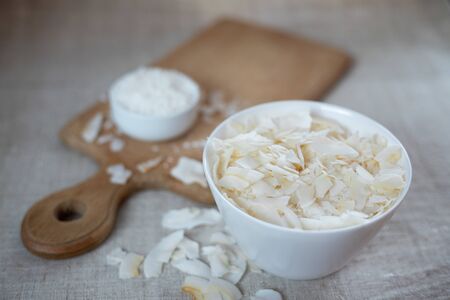 Coconut chips and shavings in a bowl on a cloth tablecloth and cutting boardの写真素材