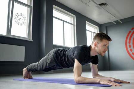 A young man stands in a plank on the elbows in the gym. Men's workout.の写真素材