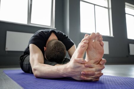 Young man doing leg stretching exercises on a yoga mat in the gym.の写真素材